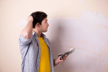 Evdeki duvara alçı yapıştıran genç adam.