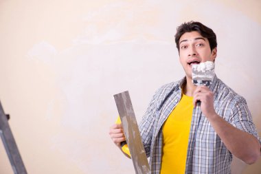 Evdeki duvara alçı yapıştıran genç adam.