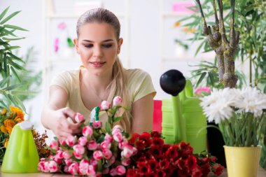Bahçesinde çiçekleri sulayan genç bir kadın.