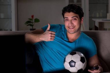 Genç adam gece geç saatlerde futbol seyrediyor.
