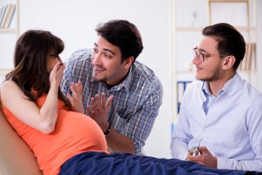 Hamile kadın kocasıyla klinikteki doktoru ziyaret ediyor.