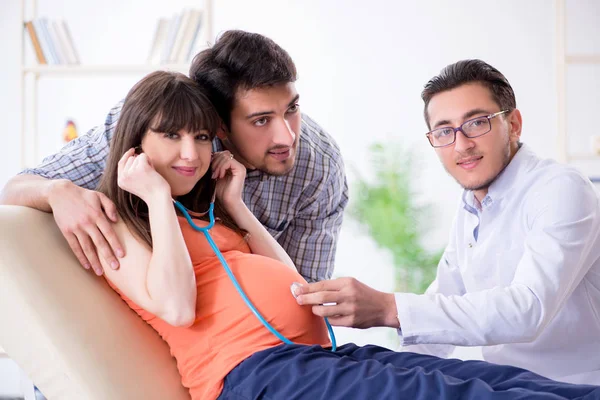 Hamile kadın kocasıyla klinikteki doktoru ziyaret ediyor.