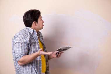 Evdeki duvara alçı yapıştıran genç adam.