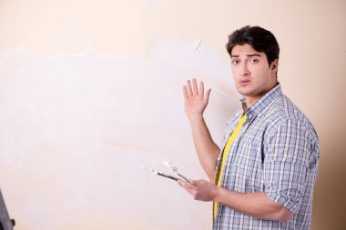 Evdeki duvara alçı yapıştıran genç adam.