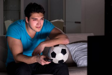 Genç adam gece geç saatlerde futbol seyrediyor.