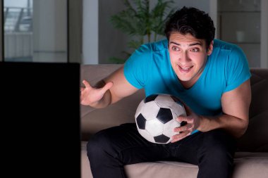 Genç adam gece geç saatlerde futbol seyrediyor.