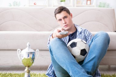 Evde futbol izleyen genç bir öğrenci.
