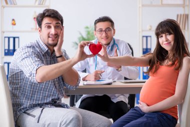 Hamile kadın kocasıyla klinikteki doktoru ziyaret ediyor.