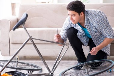 Evde bisiklet tamir eden genç bir adam.