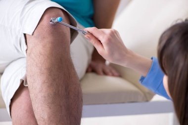 Doktor çekiçle sinir reflekslerini kontrol ediyor