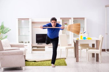 Genç adam yerleri süpürgeyle temizliyor.