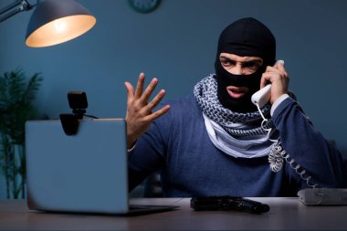 Terrorist burglar with gun working at computer clipart