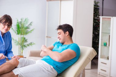 Doktor çekiçle sinir reflekslerini kontrol ediyor