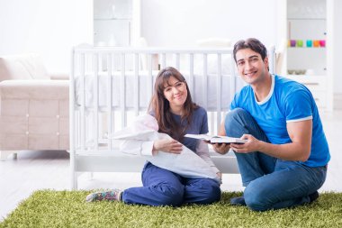 Yeni doğmuş bebekleriyle halıda oturan genç ebeveynler. 