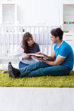 Yeni doğmuş bebekleriyle halıda oturan genç ebeveynler. 