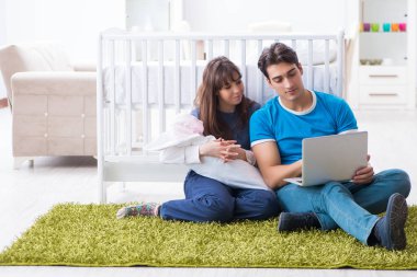 Yeni doğmuş bebekleriyle halıda oturan genç ebeveynler. 