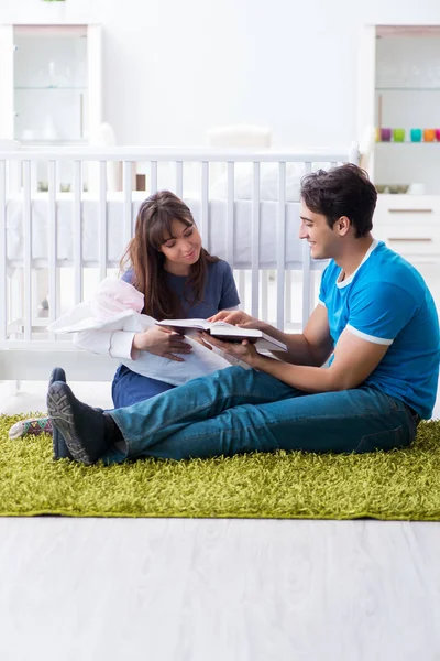 Yeni doğmuş bebekleriyle halıda oturan genç ebeveynler. 