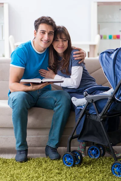 Unga föräldrar med sitt nyfödda barn i barnvagn sitter i soffan — Stockfoto