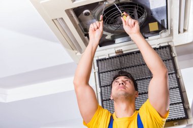 Tamirci tavan havalandırma ünitesini tamir ediyor.