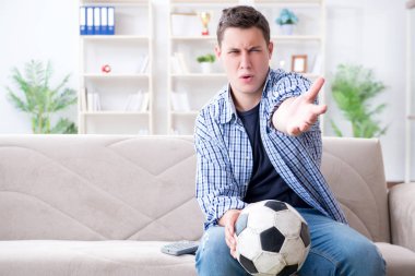 Evde futbol izleyen genç bir öğrenci.