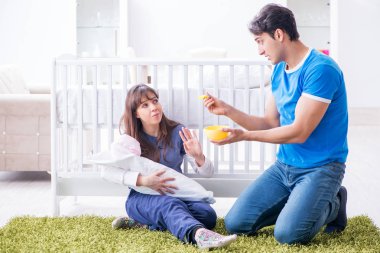 Yeni doğmuş bebekleriyle halıda oturan genç ebeveynler. 