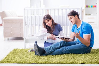 Yeni doğmuş bebekleriyle halıda oturan genç ebeveynler. 