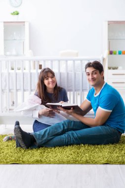 Yeni doğmuş bebekleriyle halıda oturan genç ebeveynler. 