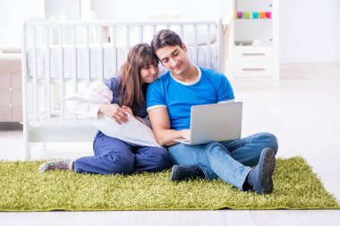 Yeni doğmuş bebekleriyle halıda oturan genç ebeveynler. 