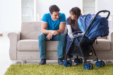 Bebekleri bebek arabasında kanepede oturan genç ebeveynler. 