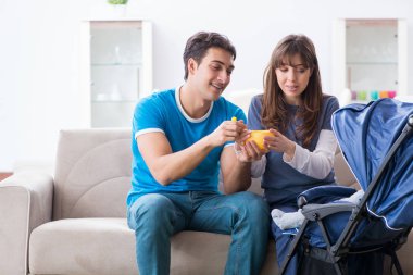 Bebekleri bebek arabasında kanepede oturan genç ebeveynler. 