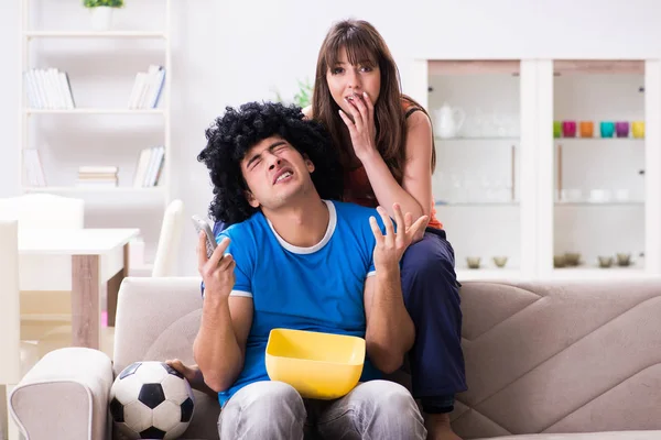 Jovem assistindo futebol com sua esposa em casa — Fotografia de Stock