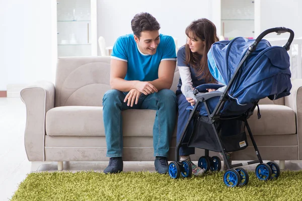 Unga föräldrar med sitt nyfödda barn i barnvagn sitter i soffan — Stockfoto