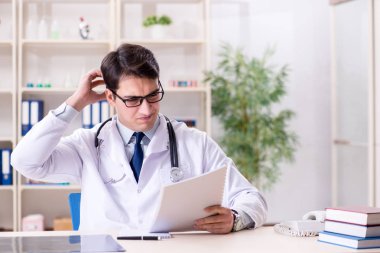 Genç doktor ofiste oturuyor.