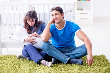 Yeni doğmuş bebekleriyle halıda oturan genç ebeveynler. 