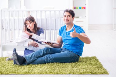 Yeni doğmuş bebekleriyle halıda oturan genç ebeveynler. 