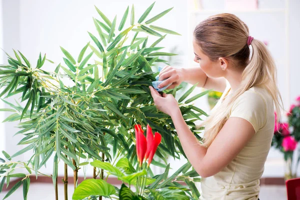 Bahçesinde çiçekleri sulayan genç bir kadın.