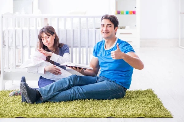 Yeni doğmuş bebekleriyle halıda oturan genç ebeveynler. 