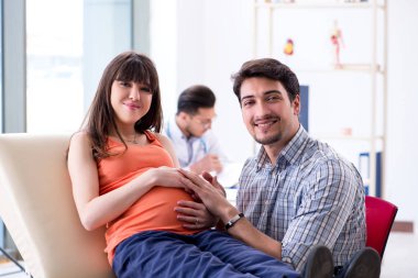Hamile kadın kocasıyla klinikteki doktoru ziyaret ediyor.