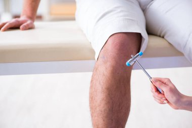 Doktor çekiçle sinir reflekslerini kontrol ediyor