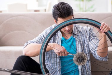 Evde bisiklet tamir eden genç bir adam.