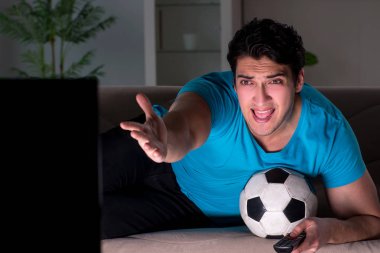 Genç adam gece geç saatlerde futbol seyrediyor.
