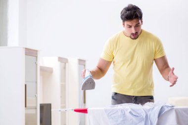 Yakışıklı koca evde kıyafet ütülüyor.