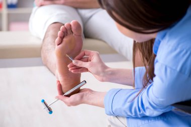 Doktor çekiçle sinir reflekslerini kontrol ediyor