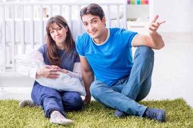 Yeni doğmuş bebekleriyle halıda oturan genç ebeveynler. 