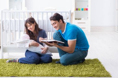 Yeni doğmuş bebekleriyle halıda oturan genç ebeveynler. 