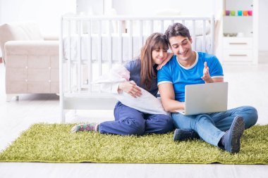 Yeni doğmuş bebekleriyle halıda oturan genç ebeveynler. 