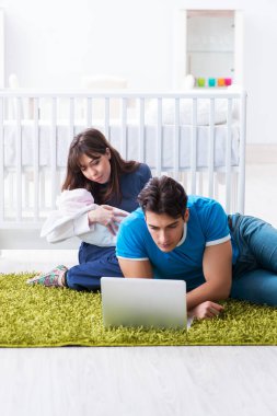 Yeni doğmuş bebekleriyle halıda oturan genç ebeveynler. 