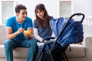 Bebekleri bebek arabasında kanepede oturan genç ebeveynler. 