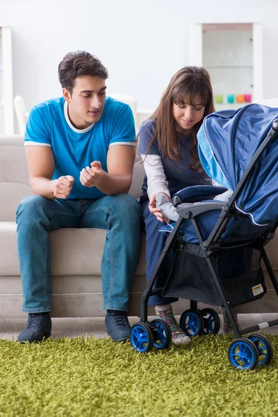 Unga föräldrar med sitt nyfödda barn i barnvagn sitter i soffan — Stockfoto