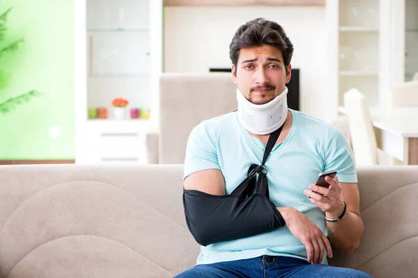 Jeune étudiant homme avec cou et blessure à la main assis sur le canapé — Photo